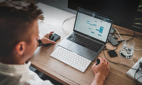 zan-AmEeEB1g3XQ-unsplash-mobile-500x300px Mann mit Handy guckt seinen Laptop