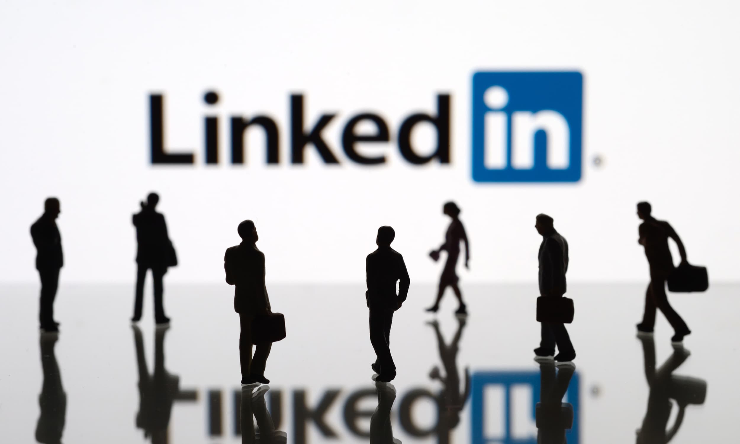 Silhouetten von Geschäftsleuten mit Koffern vor dem LinkedIn-Logo das im Hintergrund unscharf zu sehen ist