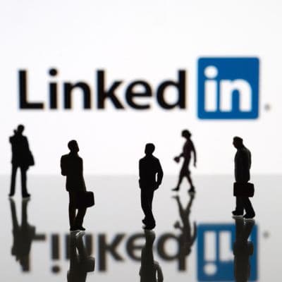 Silhouetten von Geschäftsleuten mit Koffern vor dem LinkedIn-Logo das im Hintergrund unscharf zu sehen ist